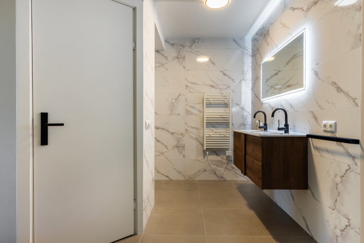 Moderne badkamer met dubbele wastafel en marmeren tegels in vakantiehuis Boszicht 16a Schiermonnikoog