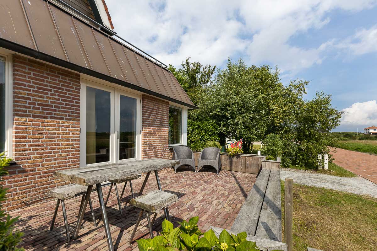 Vooraanzicht van vakantiehuis Boszicht 16a Schiermonnikoog met bomen en zonlicht